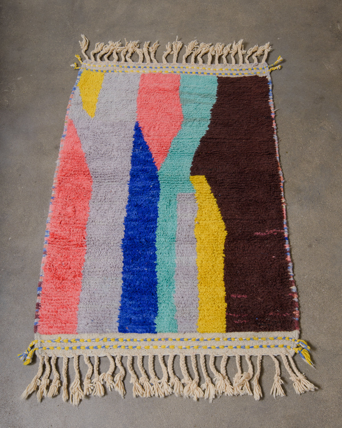Berberlin special edition Beniourain rug made of colourful wool in coral pink, lavender, turquoise, yellow and brown, laying on concrete studio floor.